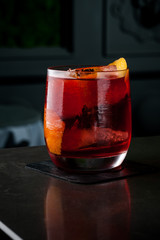 The bartender makes a cocktail of orange and ice. Macro, black background, hand, red
