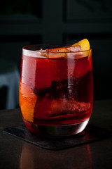 The bartender makes a cocktail of orange and ice. Macro, black background, hand, red