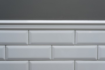 Gray painted wall, part of the wall is covered tiles small white glossy brick, ceramic decorative molding tiles. Fragment of the walls of the bathroom, toilet, kitchen
