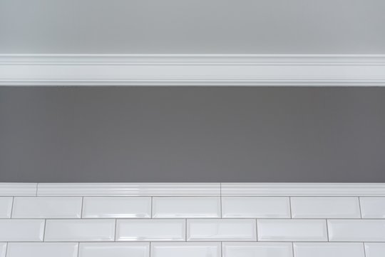 Gray painted wall, white ceiling molding and ceramic decorative tiles small white glossy brick. Fragment of the walls of the bathroom, toilet, kitchen.