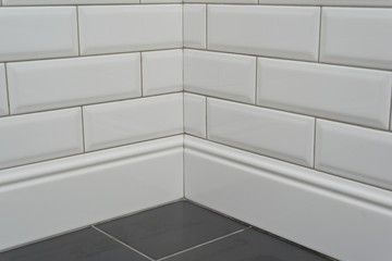 Close-up corner covered with white decorative tiles with high ceramic plinth, molding, curb, and piece of floor tile