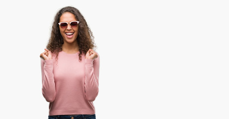 Fototapeta premium Beautiful young hispanic woman wearing sunglasses excited for success with arms raised celebrating victory smiling. Winner concept.
