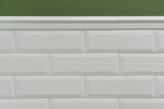 Green painted wall, part of the wall is covered tiles small white glossy brick, ceramic decorative molding tiles. Fragment of the walls of the bathroom, toilet, kitchen © Valerii Honcharuk