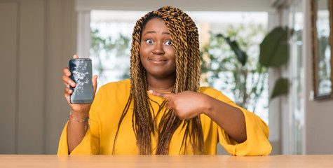 African american woman showing broken smartphone very happy pointing with hand and finger