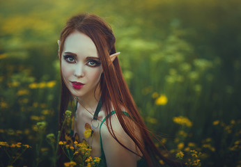 Portrait of a redheaded girl elf in a green swimsuit posing in a clearing of yellow flowers....