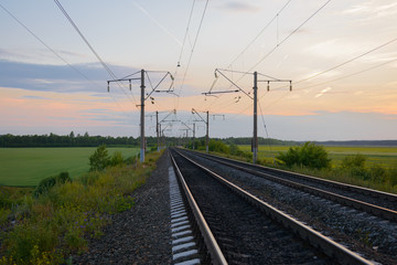 Fototapeta na wymiar railway with poles among forests and fields in the summer evening