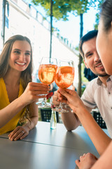 Beautiful woman and her best friends toasting with a refreshing alcoholic drink while sitting together at table outdoors in a trendy restaurant in summer