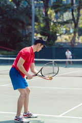 Side view of an Asian tennis player ready to serve at the beginning of a doubles mixed match on a professional tennis court