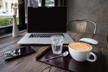 A Cup of hot heart latte art coffee on wooden plate with laptop and smart phone computer