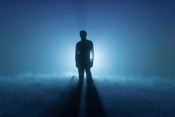 A foggy night. Blue tones. Silhouette of a man. Spotlight behind a man