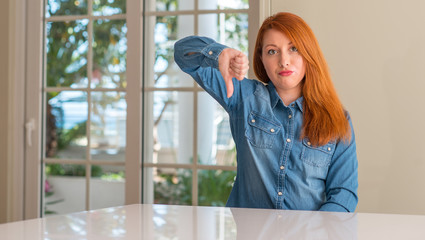 Redhead woman at home with angry face, negative sign showing dislike with thumbs down, rejection...