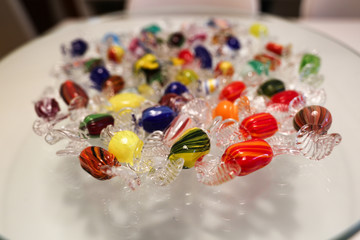 Colorful candies made of glass are lying on a transparent plate.