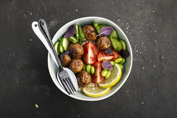 A healthy, balanced, healthy diet. Meat balls, tomatoes, rice, cucumbers, soy beans, spinach, lemon, bowl. Top View.