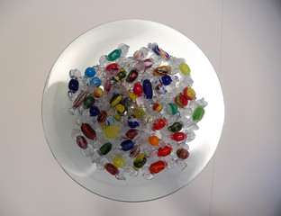 Colorful candies made of glass are lying on a transparent plate.