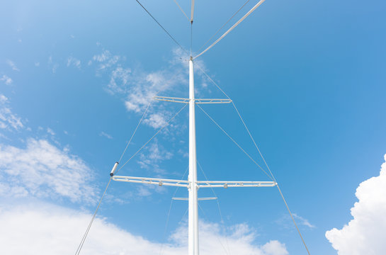 White metal mast of a ship without sails on the background of the bright sky