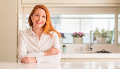 Redhead woman at kitchen happy face smiling with crossed arms looking at the camera. Positive person.