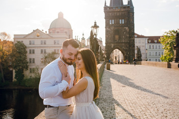 Close up happy groom and bride hugging and smiling while walking on the Charles bridge on sunset....