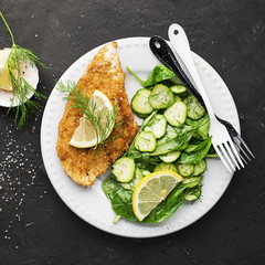 Chicken Milanese with fresh cucumbers, spinach, dill, butter and pink salt on a white plate on the table. Top View