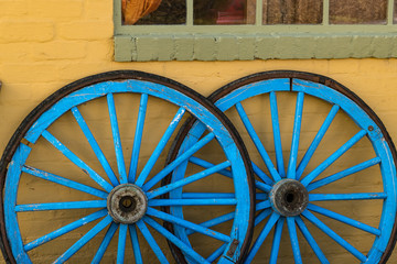 A pair of blue wagon wheels leaning against a yellow wall