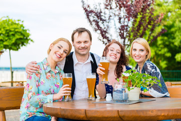 Happy friends toasting with beer in garden restaurant