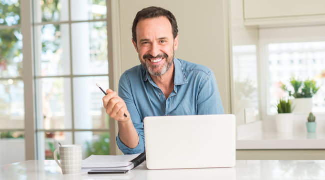 Middle age man using laptop at home with a happy face standing and smiling with a confident smile showing teeth