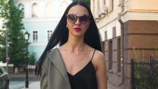 Young stylish woman wearing sunglasses walk on camera in slow motion