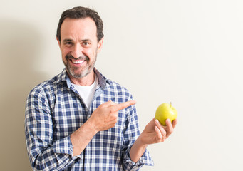 Senior man holding a green apple very happy pointing with hand and finger to the side