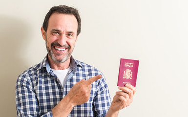 Senior man holding spanish passport very happy pointing with hand and finger to the side