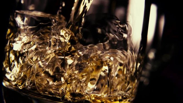 Slow motion amber bourbon pour into a glass with ice on a black background at an incline