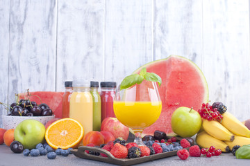 Juice in bottles, different and in a glass. Assorted berries and fruits. Gray background. Detox food. Copy space,