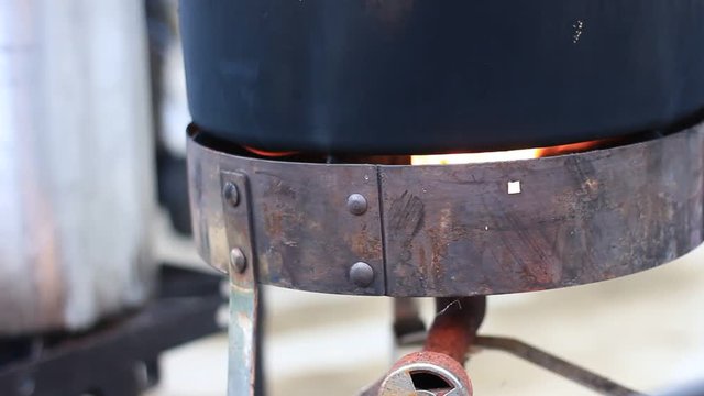 Burner with a flame under a large metal pot of crab.