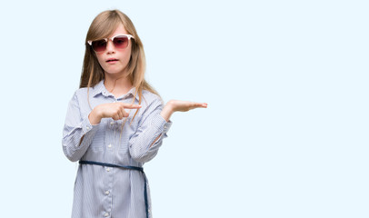 Young blonde toddler wearing blue shirt very happy pointing with hand and finger