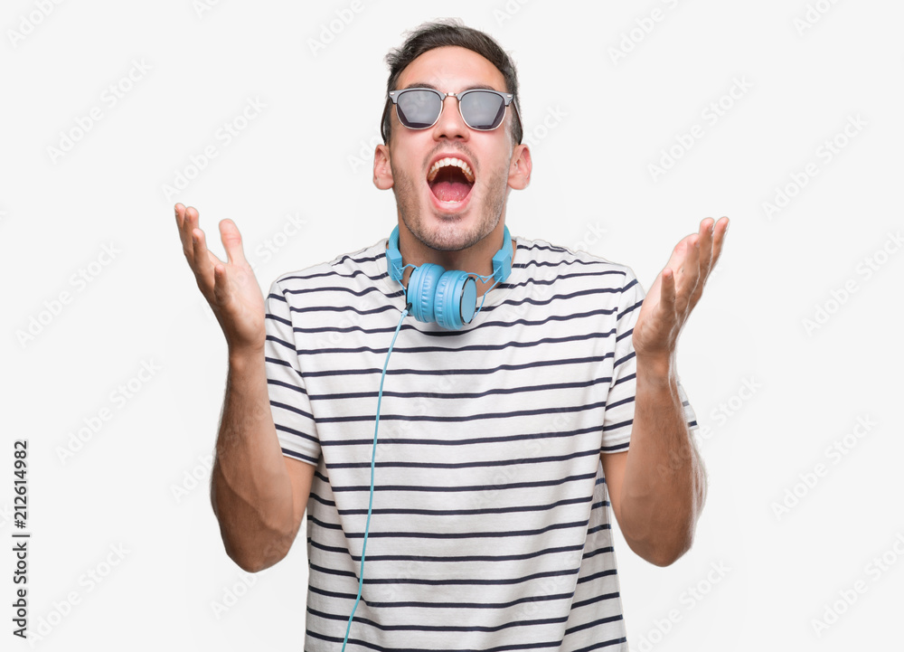 Poster handsome young man wearing headphones crazy and mad shouting and yelling with aggressive expression 