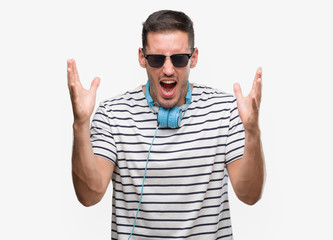 Naklejka premium Handsome young man wearing headphones celebrating mad and crazy for success with arms raised and closed eyes screaming excited. Winner concept
