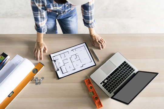 woman civil architech engineer checking blueprint or home plan with laptop on wood table,engineering and architecture concept.Blue print is fake only for stock photo.
