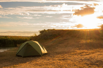 Green tent of hikers near river during the sunset or sunrise