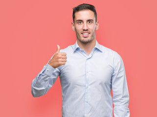 Handsome young businessman doing happy thumbs up gesture with hand. Approving expression looking at...