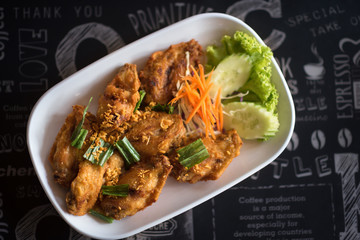 Top view thai style fried chicken wings on a round white plate on a wood table