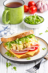 Ham sandwich with scrambled egg, cheese, tomato, lettuce, tasty healthy Breakfast on white wooden background