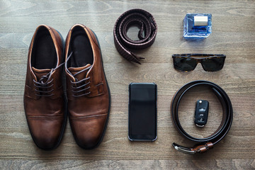 Different men's accessories such as: shoes, belt, tie, glasses, car keys and telephone - are on the table