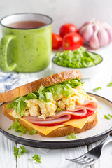 Ham sandwich with scrambled egg, cheese, tomato, lettuce, tasty healthy Breakfast on white wooden background
