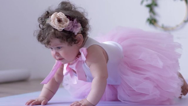child girl in pink dress crawling on white background indoors on a photo session