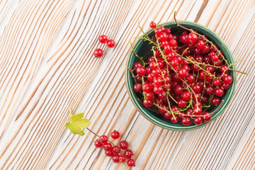 Close up top view of green cup with red currant berry and small bunch of red currant with green leaf of currant bush in front of cup isolated on white wood background. Summer concept with copy space.