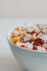 Healthy fruit salad. Bowl with pomegranate seeds, mango, coconut flakes, tangerine, dried apricot and walnut