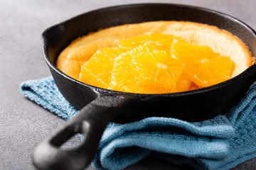 Delicious dutch baby pancake baked in oven in cast-iron frying pan with orange slices in honey on gray concrete background. Healthy breakfast concept with copy space.