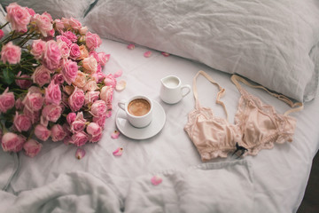 Gently pink roses lie on the gray linen bedding with coffee. Romantic mood of the morning