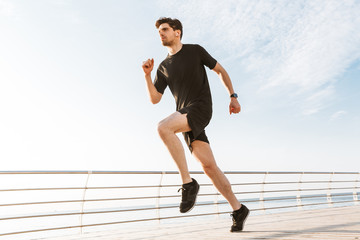 Handsome young sportsman running outdoors listening music