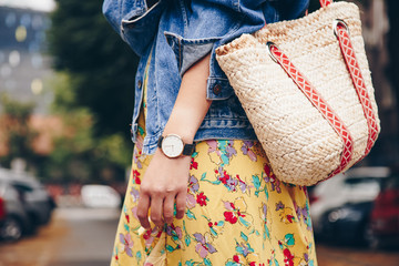 street style fashion details. woman wearing a summer dress and a white and black analog wrist watch, holding a trendy beach straw purse. perfect summer 2018 fashion accessories. 