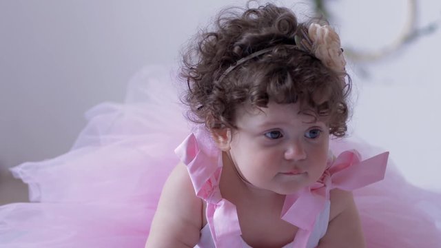 children's photo session, little girl with big eyes and curly hair in a pink dress close-up posing in white studio