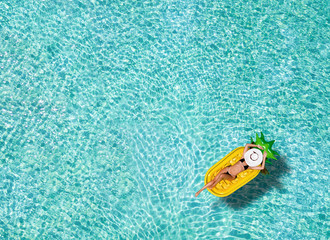 Obraz premium Junge, schlanke Frau im Bikini treibt auf einer Ananasförmigen Luftmatratze über die tropischen Gewässer der Malediven und genießt ihren Urlaub